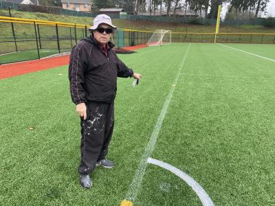 Experienced athletic field painter showing barely visible paint lines on synthetic turf and how it stands out with Turf Stress Detection Glasses
